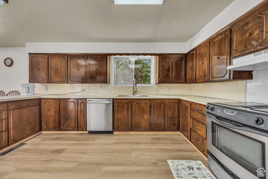 Kitchen featuring stainless steel appliances, light countertops, under cabinet range hood, light wood finished floors, and backsplash
