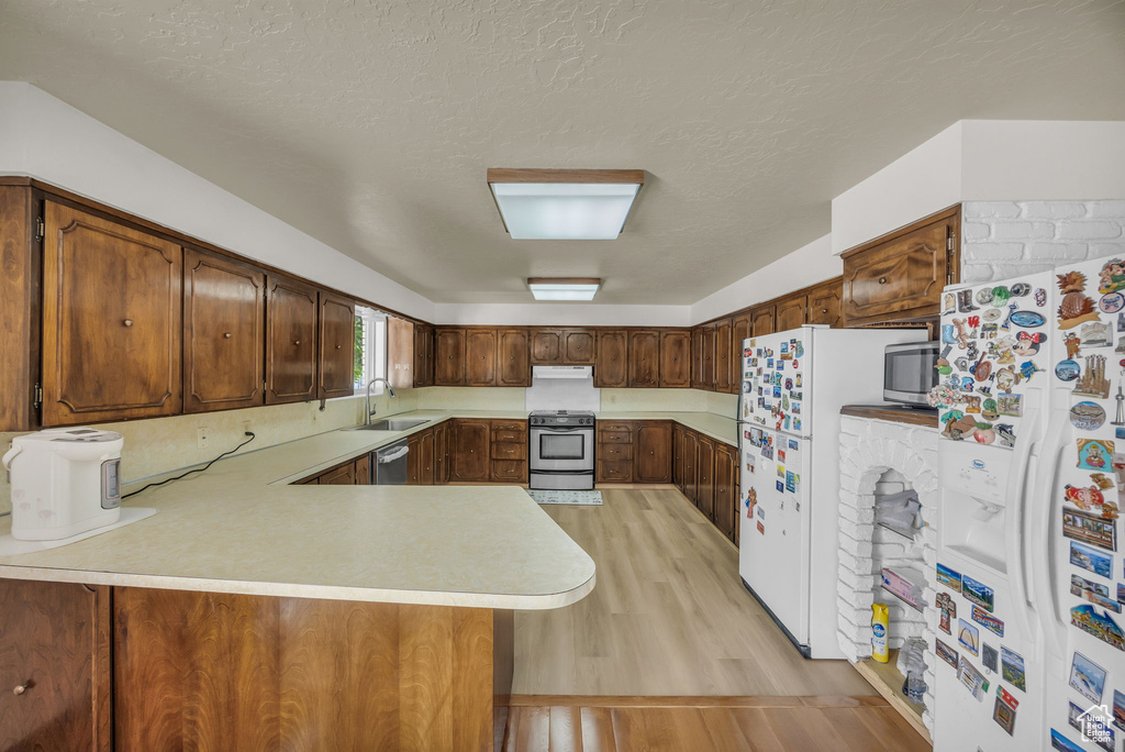 Kitchen with stainless steel appliances, light countertops, a peninsula, light wood-type flooring, and a textured ceiling