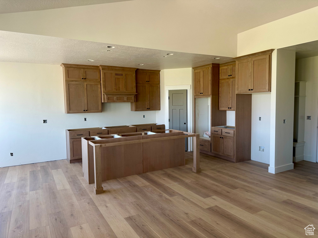 Kitchen with a center island, light wood finished floors, recessed lighting, lofted ceiling, and brown cabinets