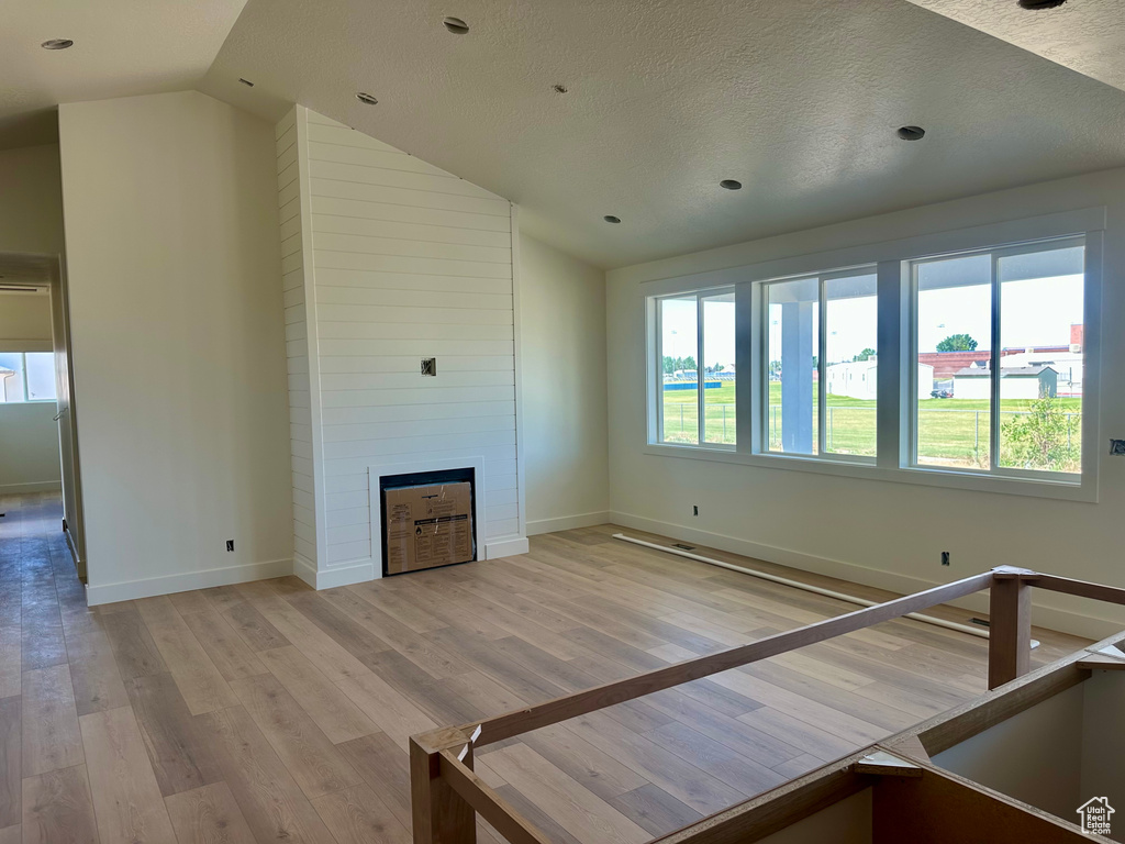Unfurnished living room featuring lofted ceiling, a fireplace, light wood-style floors, and a textured ceiling