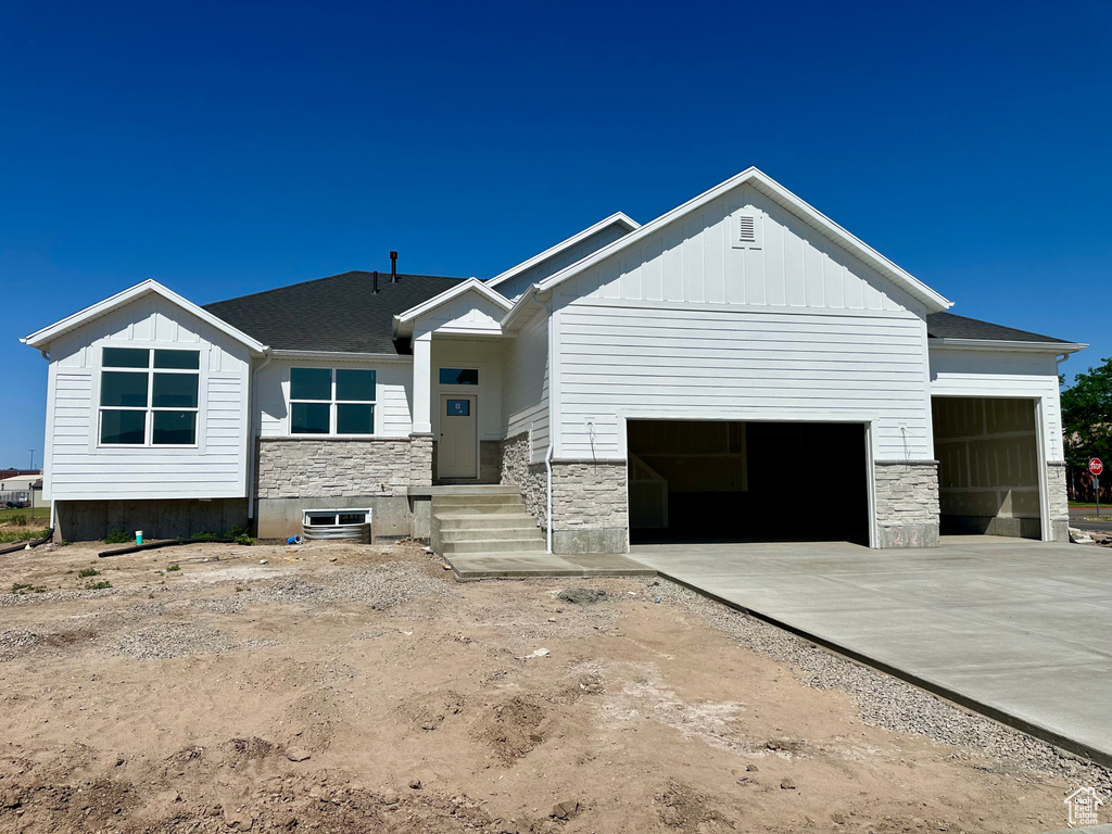 View of front of house with a garage, stone siding, board and batten siding, and driveway
