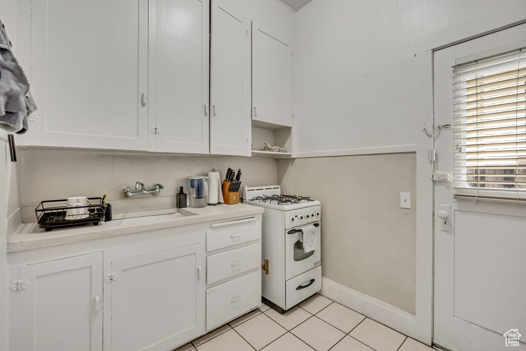 Kitchen with white gas range, white cabinets, light countertops, and light tile patterned floors