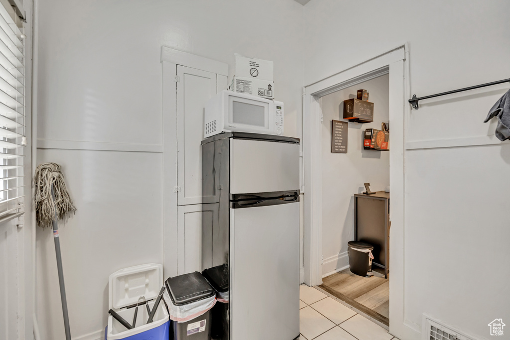 Kitchen with freestanding refrigerator, white microwave, and light tile patterned floors