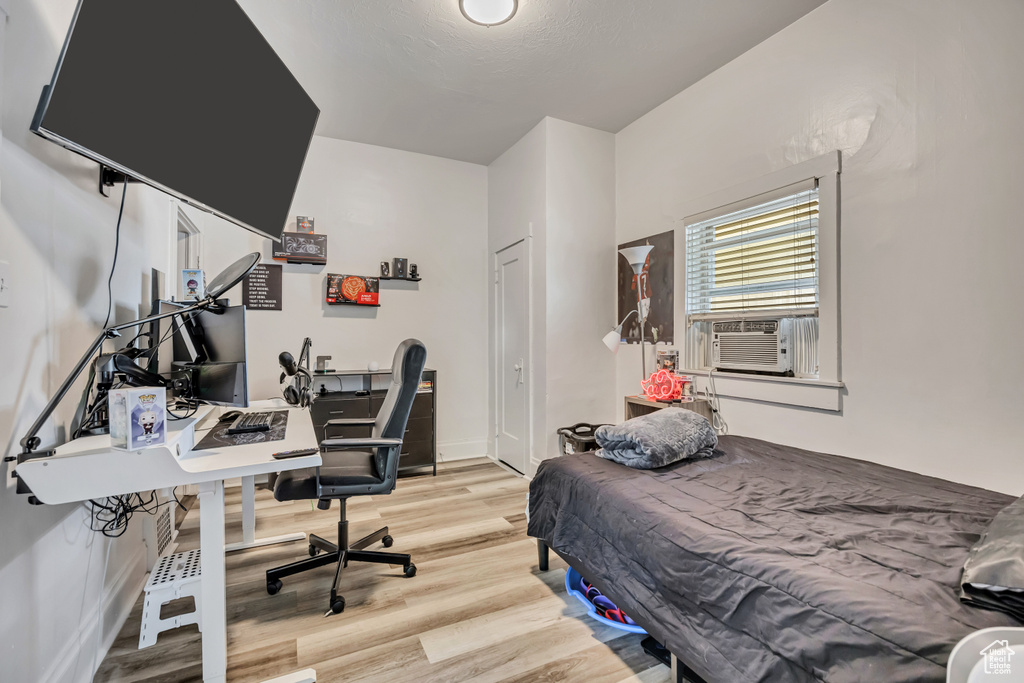 Bedroom featuring light wood finished floors, an office area, and cooling unit