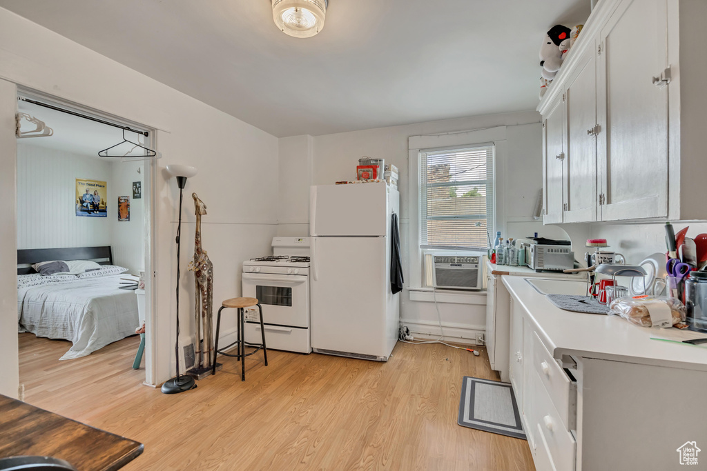 Kitchen featuring white appliances, light wood-style flooring, light countertops, cooling unit, and white cabinetry