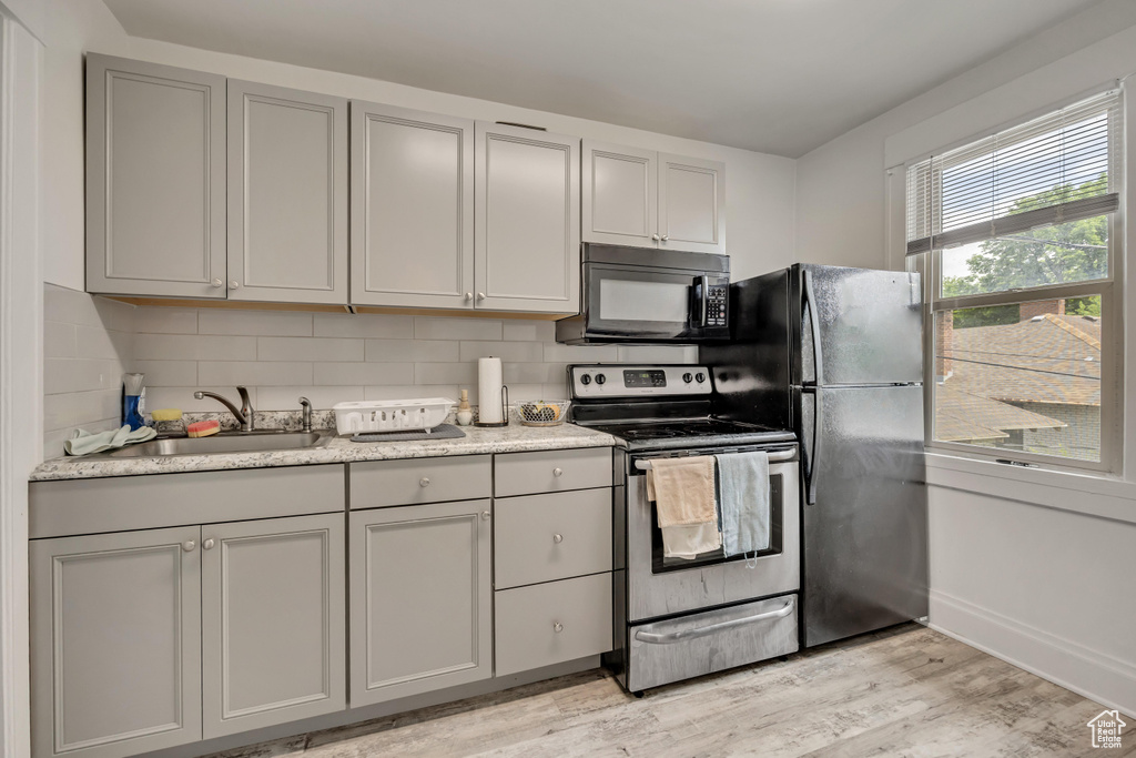 Kitchen with black appliances, gray cabinets, tasteful backsplash, light wood-type flooring, and light countertops