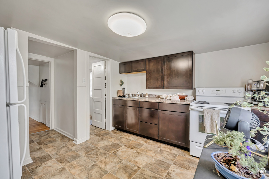 Kitchen with white appliances, dark brown cabinetry, light countertops, and stone finish floors