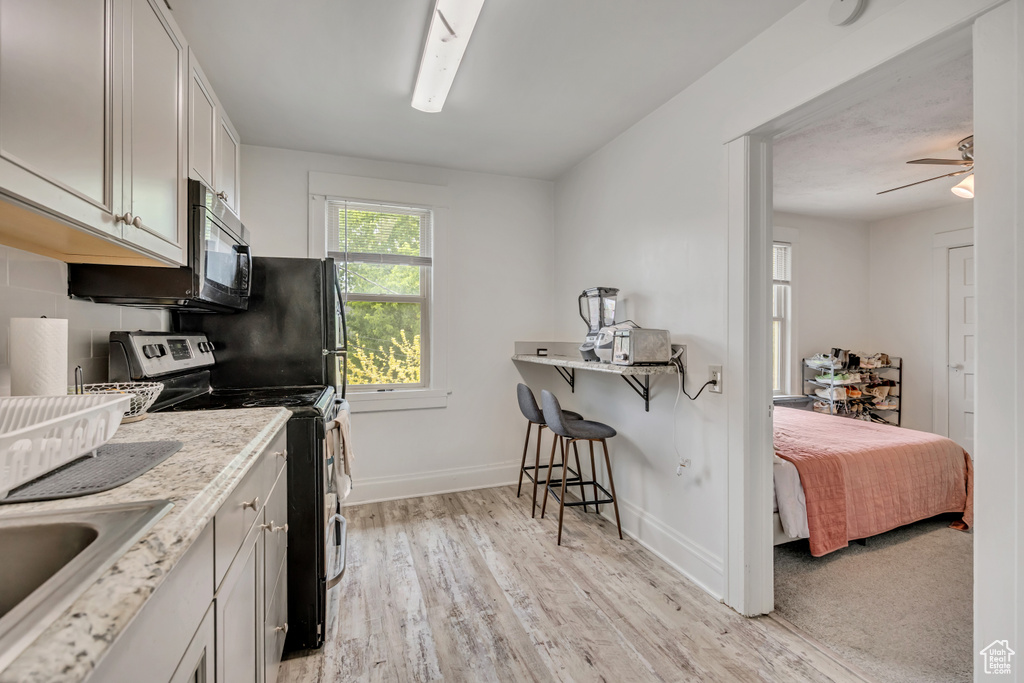 Kitchen with range with electric stovetop, light wood-style flooring, a breakfast bar area, ceiling fan, and white cabinets