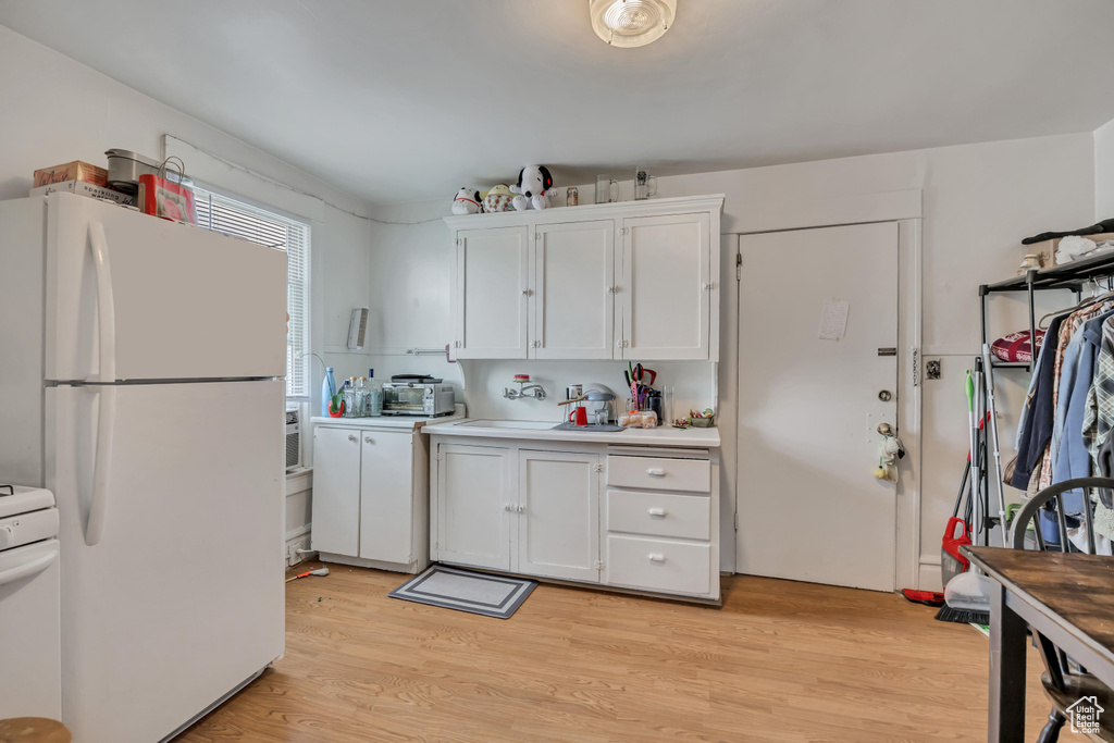 Kitchen with freestanding refrigerator, light countertops, white cabinets, stove, and light wood-type flooring