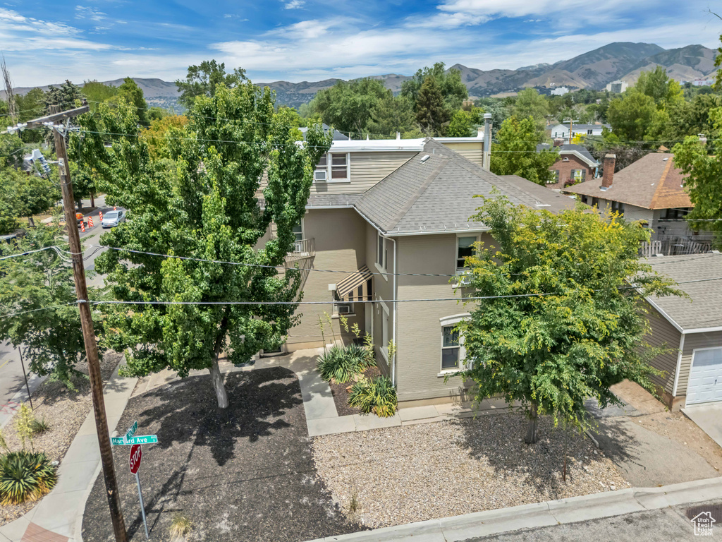 View of property hidden behind natural elements featuring stucco siding, a mountain view, and roof with shingles