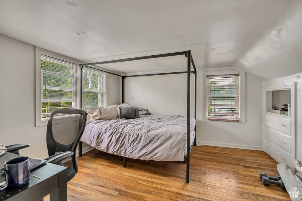 Bedroom with wood finished floors, lofted ceiling, and multiple windows