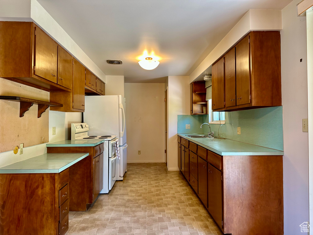 Kitchen with white electric range, open shelves, light countertops, brown cabinets, and backsplash