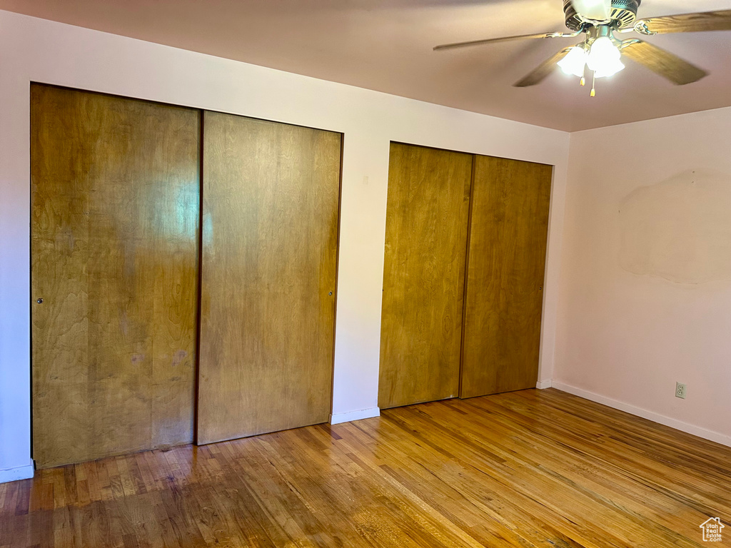 Unfurnished bedroom featuring two closets, wood finished floors, and a ceiling fan
