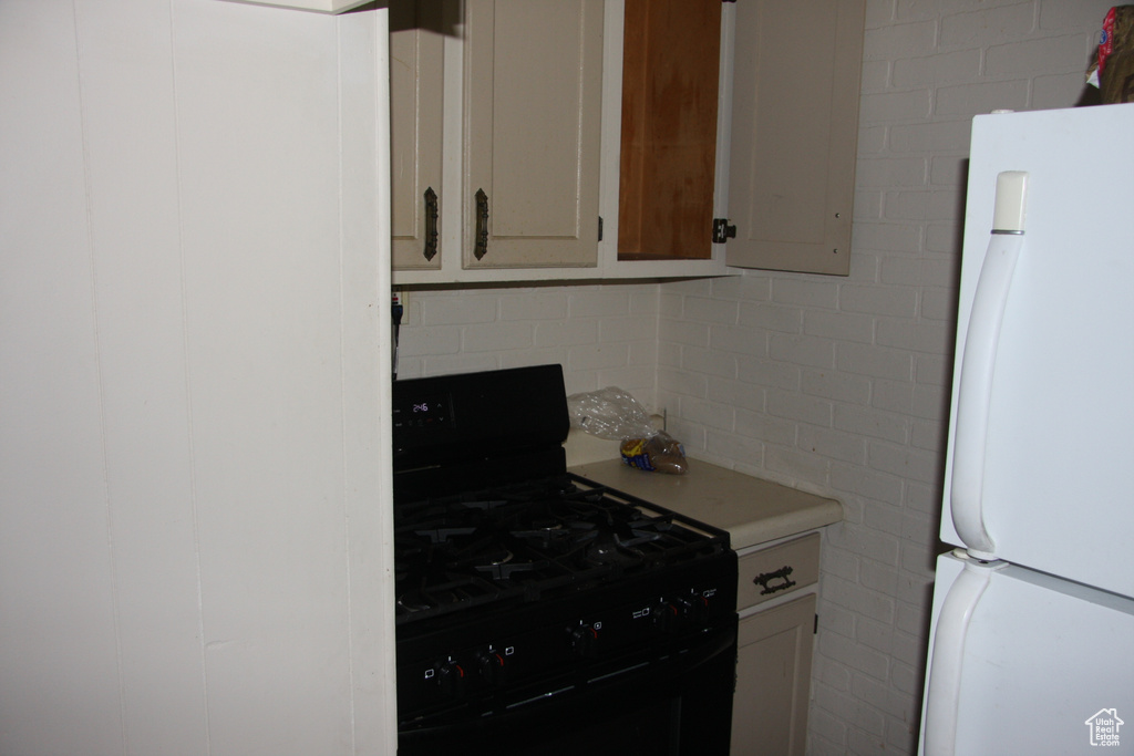 Kitchen featuring freestanding refrigerator, black gas range, light countertops, and tasteful backsplash