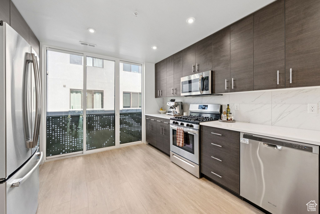 Kitchen with appliances with stainless steel finishes, dark brown cabinetry, light countertops, backsplash, and light wood-style floors