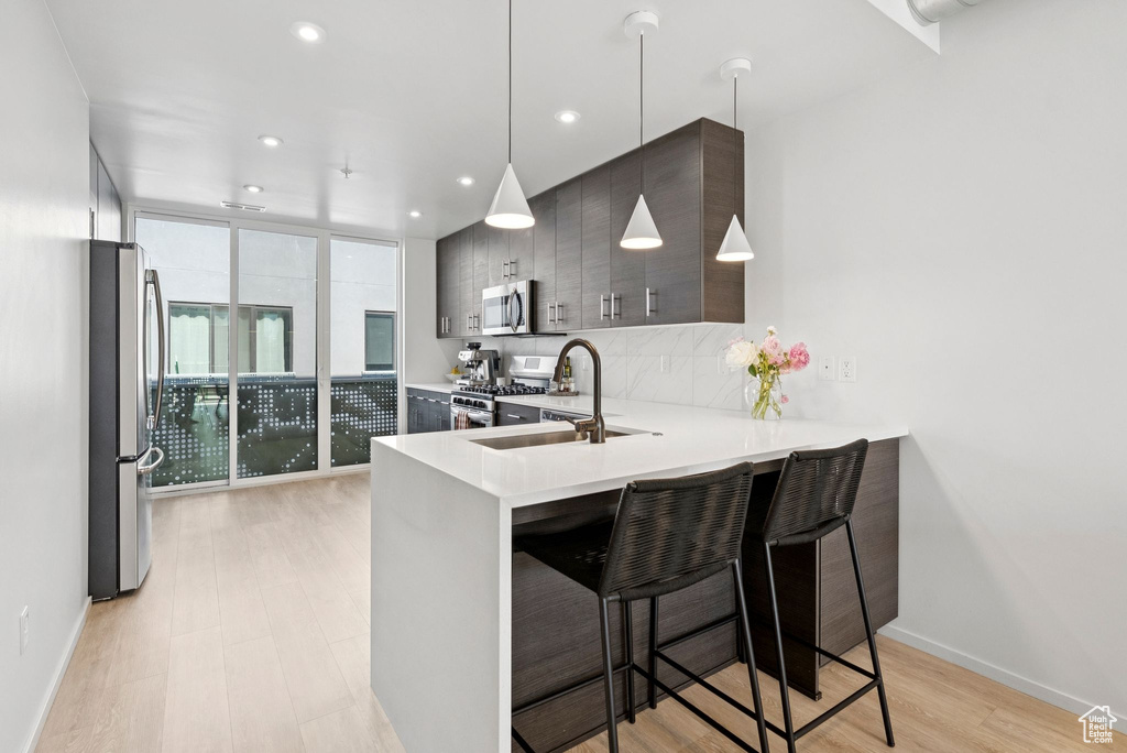 Kitchen featuring stainless steel appliances, light countertops, a kitchen breakfast bar, light wood finished floors, and a peninsula