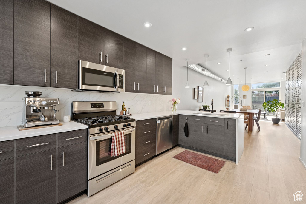 Kitchen featuring appliances with stainless steel finishes, a peninsula, light countertops, backsplash, and recessed lighting
