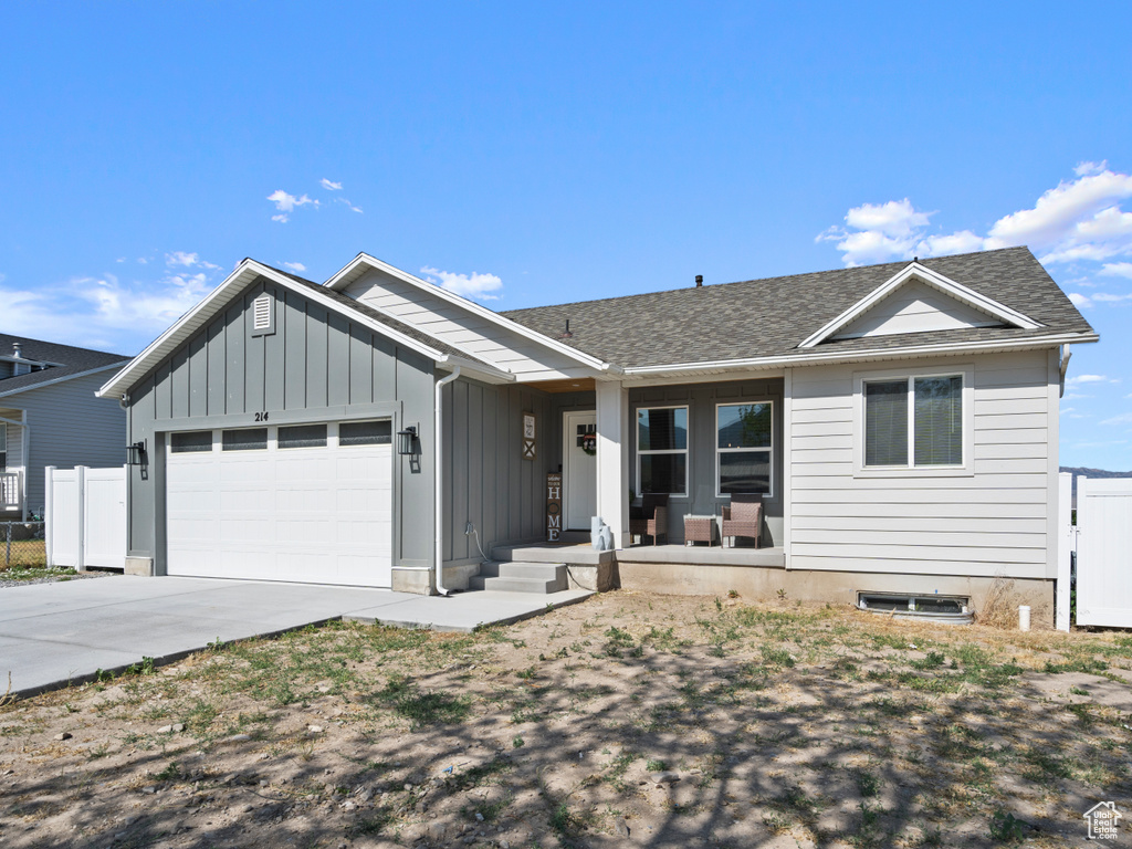 Single story home featuring an attached garage, board and batten siding, concrete driveway, a porch, and a shingled roof