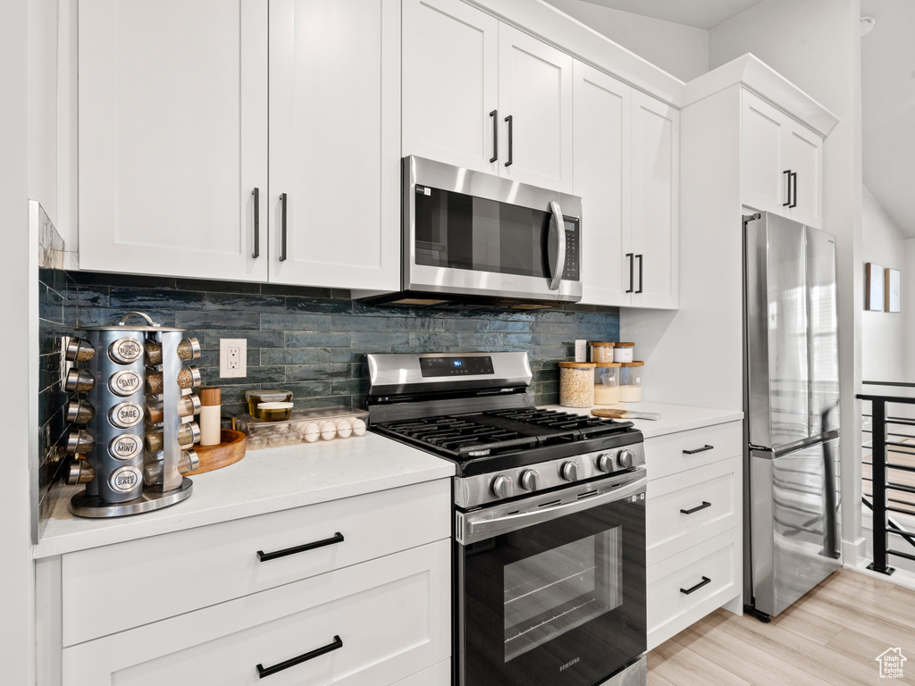Kitchen featuring appliances with stainless steel finishes, light countertops, white cabinets, backsplash, and light wood-style floors