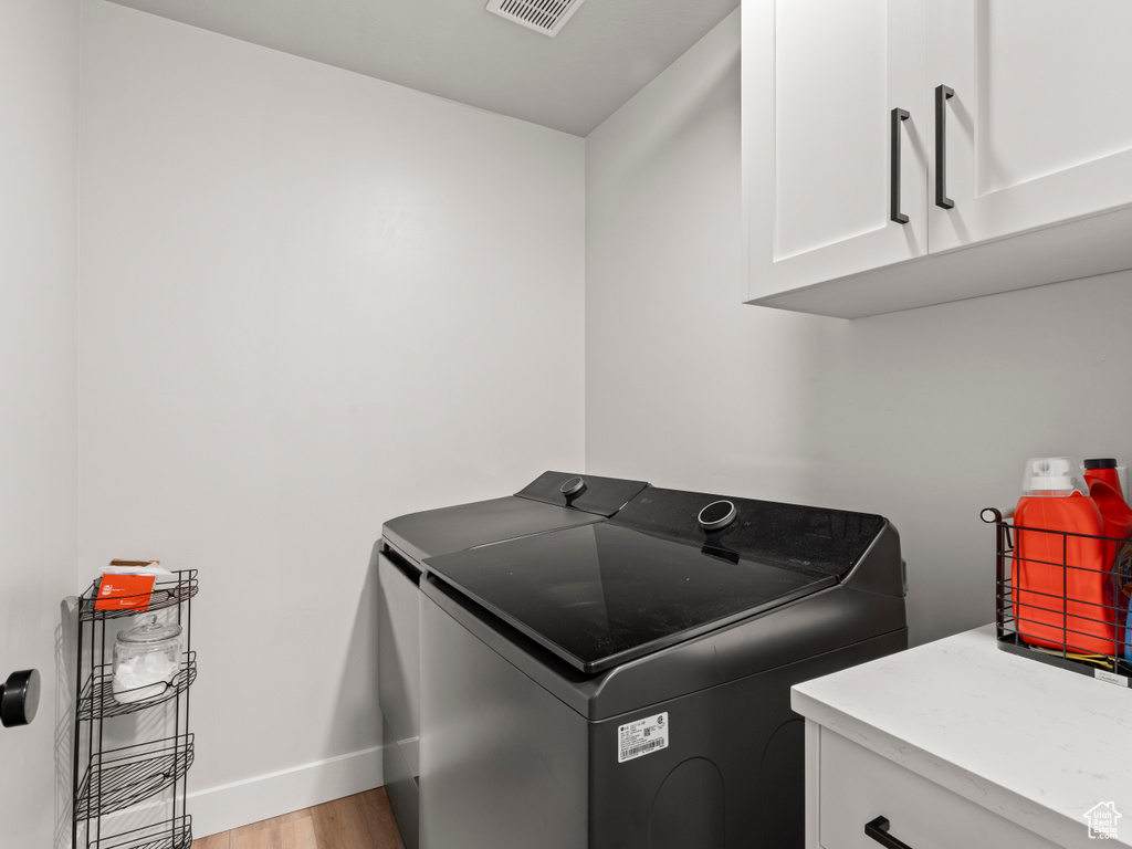 Washroom with cabinet space, washer and dryer, and light wood-style flooring