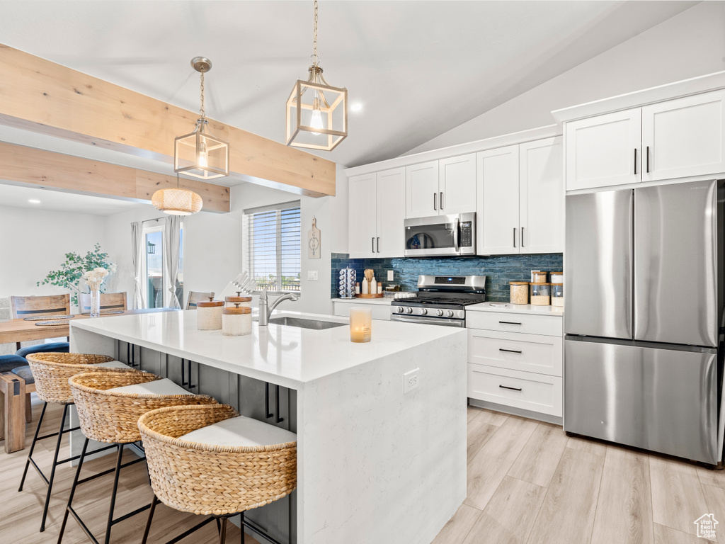 Kitchen with stainless steel appliances, decorative backsplash, a breakfast bar area, light countertops, and white cabinetry