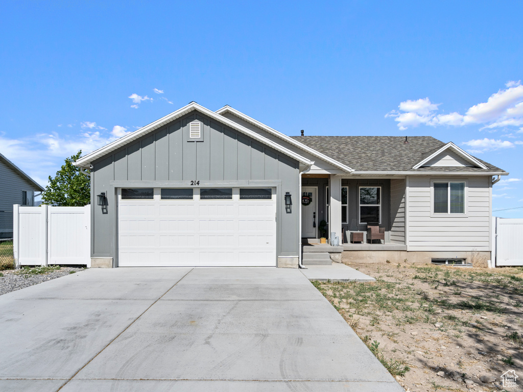 Single story home with an attached garage, concrete driveway, covered porch, board and batten siding, and roof with shingles