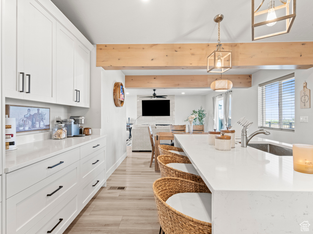Kitchen featuring light countertops, white cabinetry, beam ceiling, decorative light fixtures, and open floor plan