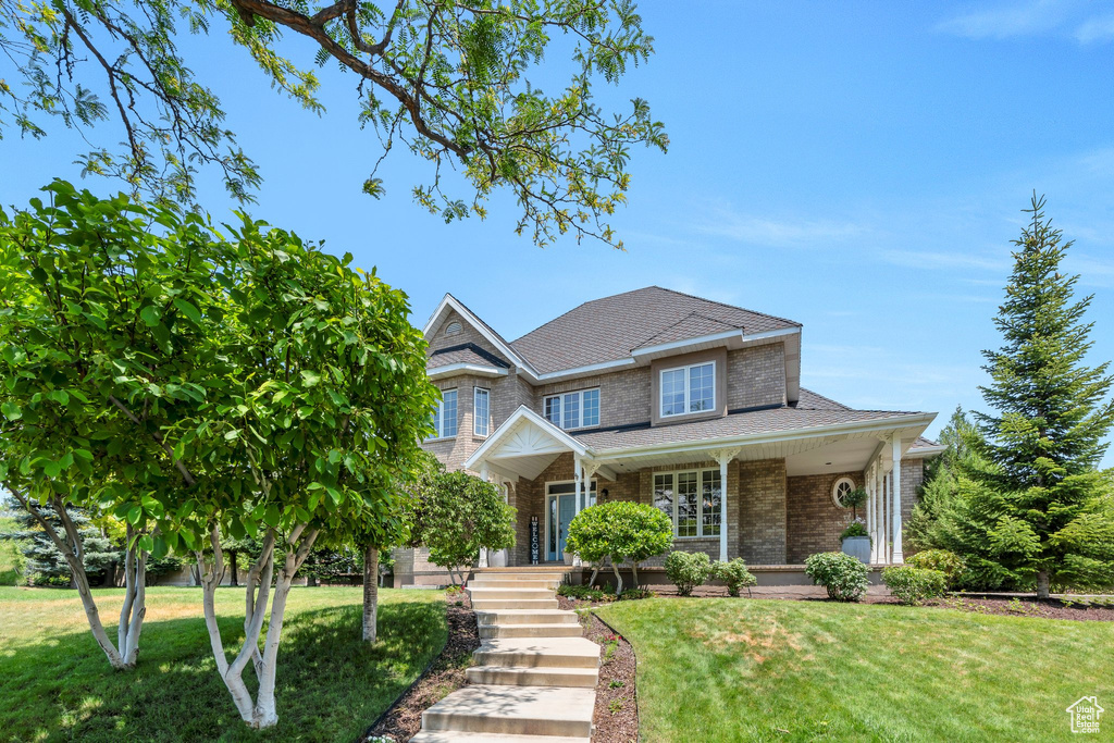 View of front facade with a front lawn, brick siding, a shingled roof, and a porch