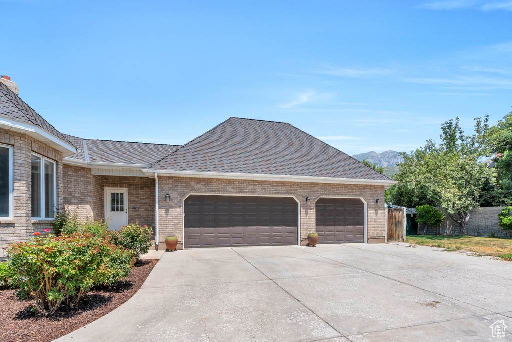 View of front facade featuring a garage, driveway, brick siding, a mountain view, and roof with shingles