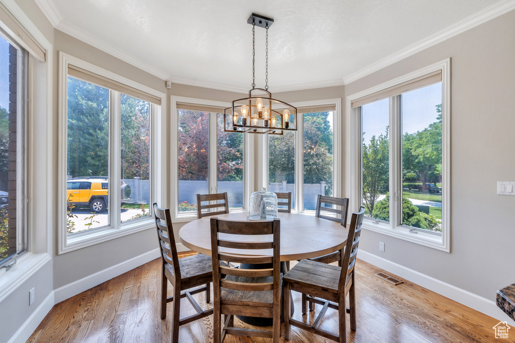 Dining space featuring healthy amount of natural light, light wood-style floors, ornamental molding, and a chandelier