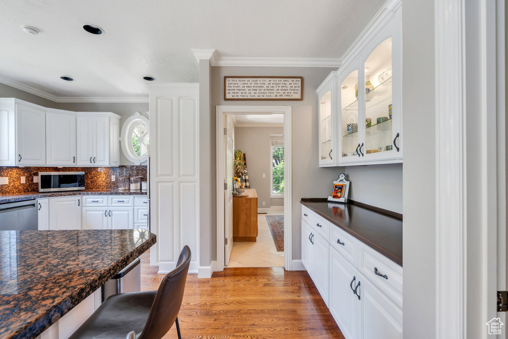 Kitchen with appliances with stainless steel finishes, dark countertops, crown molding, white cabinets, and glass insert cabinets