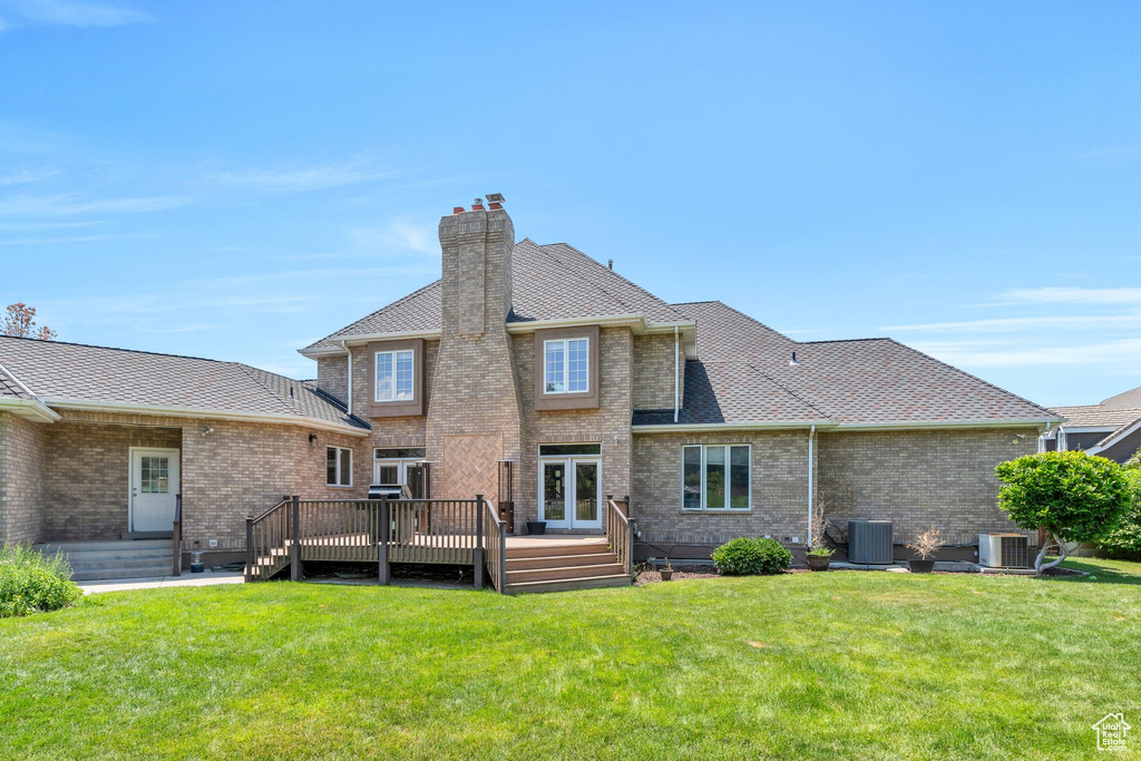 Back of property with a deck, a lawn, a chimney, and brick siding