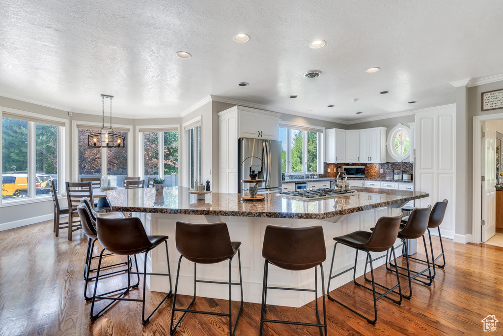 Kitchen featuring appliances with stainless steel finishes, crown molding, white cabinetry, a large island, and light wood-type flooring