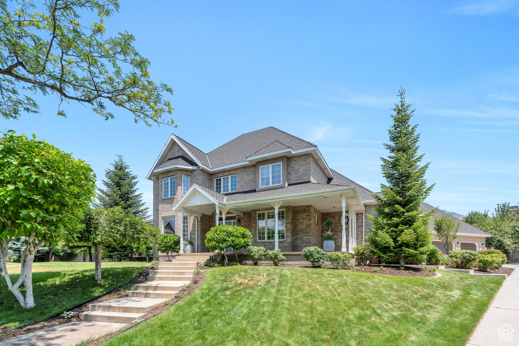 View of front of property featuring a front lawn, brick siding, and covered porch
