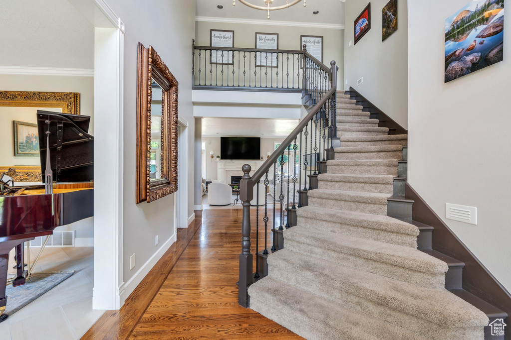 Foyer entrance with crown molding, stairs, wood finished floors, a fireplace, and a high ceiling