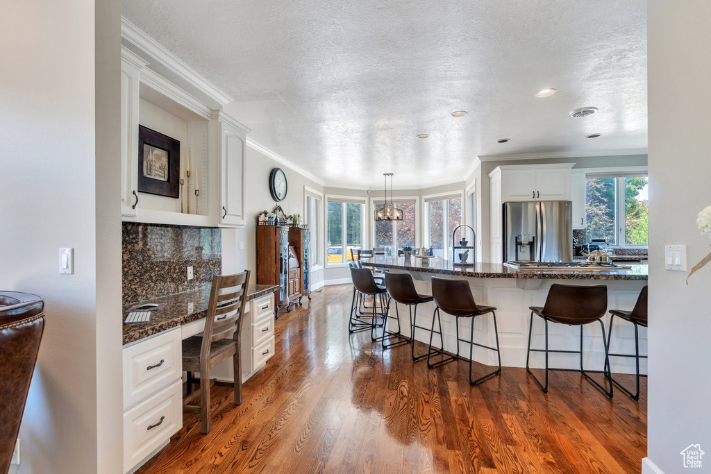 Kitchen with appliances with stainless steel finishes, a kitchen bar, white cabinets, crown molding, and decorative backsplash