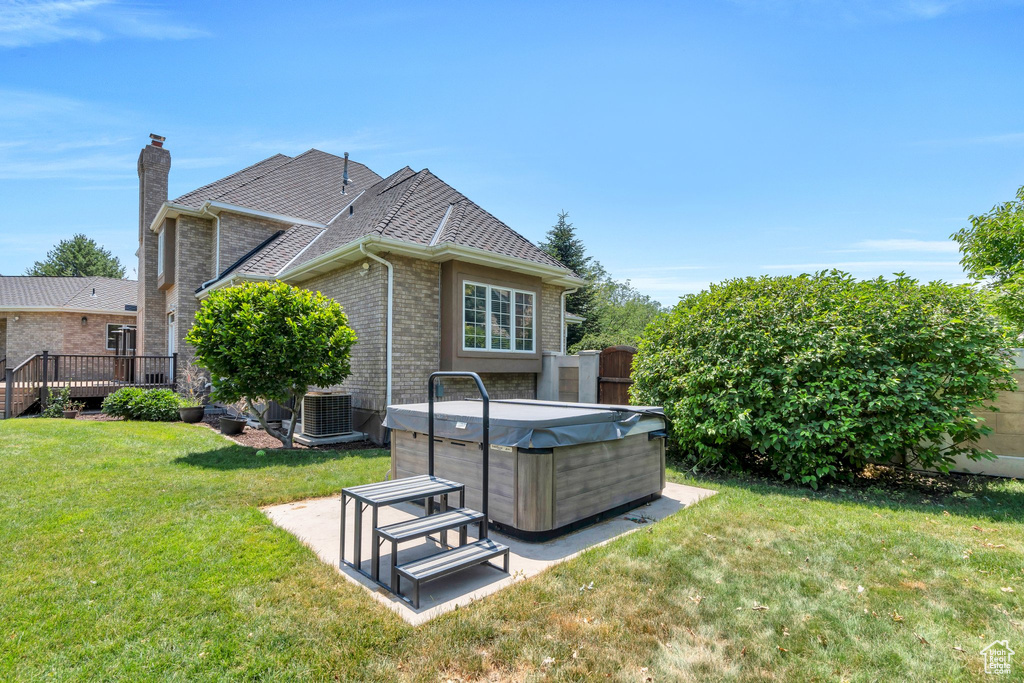 Back of house with a hot tub, a chimney, brick siding, and a wooden deck