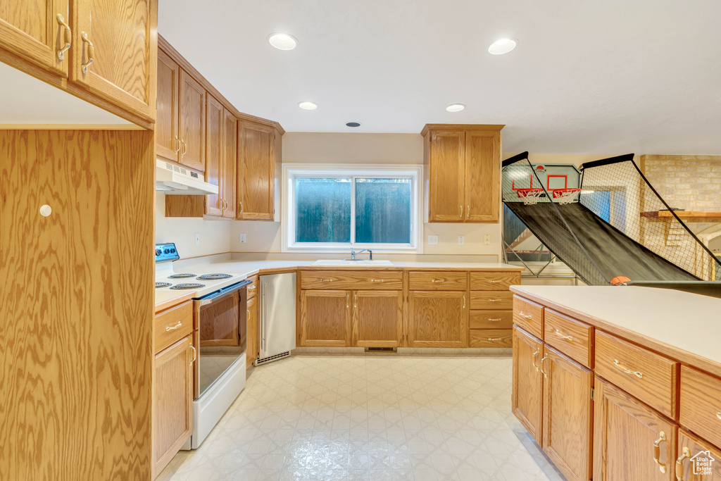 Kitchen with white range with electric cooktop, under cabinet range hood, light countertops, light floors, and dishwasher