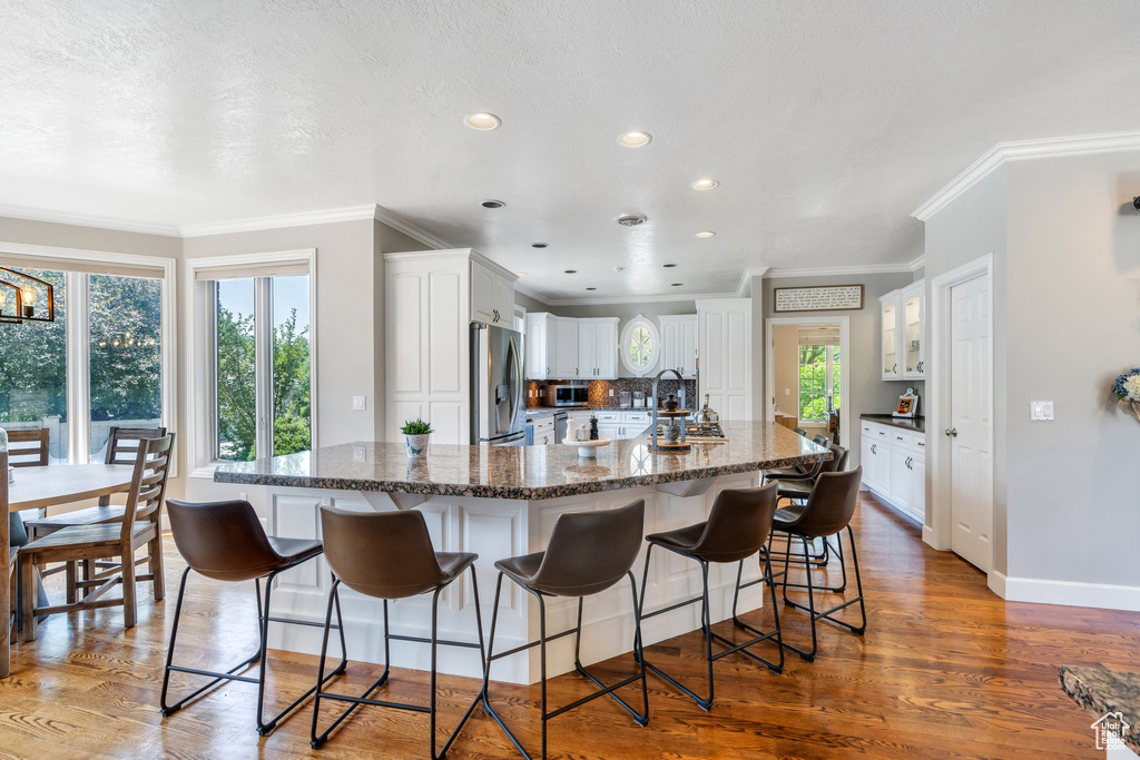Kitchen featuring stainless steel appliances, ornamental molding, white cabinets, a breakfast bar area, and wood finished floors