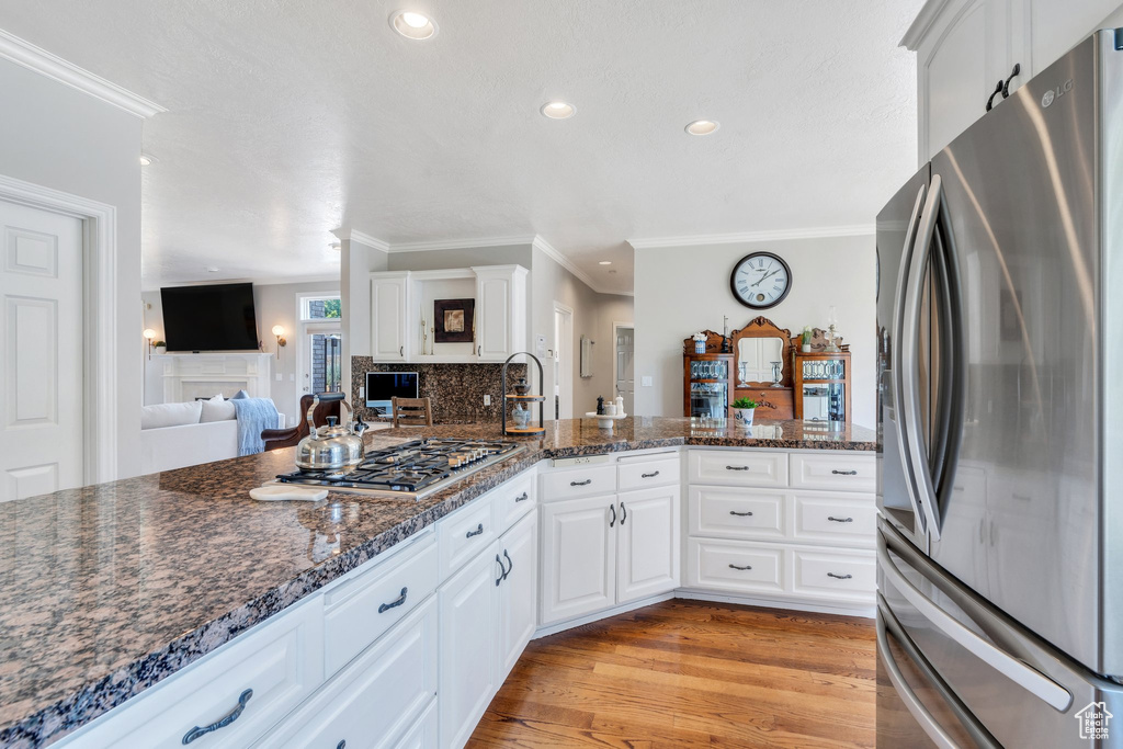 Kitchen with stainless steel appliances, ornamental molding, light wood-style floors, white cabinets, and dark stone counters
