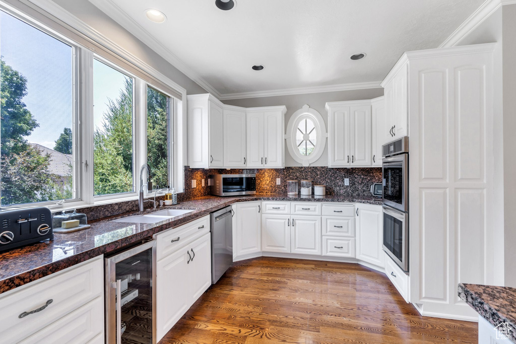 Kitchen with wine cooler, stainless steel appliances, white cabinets, backsplash, and crown molding