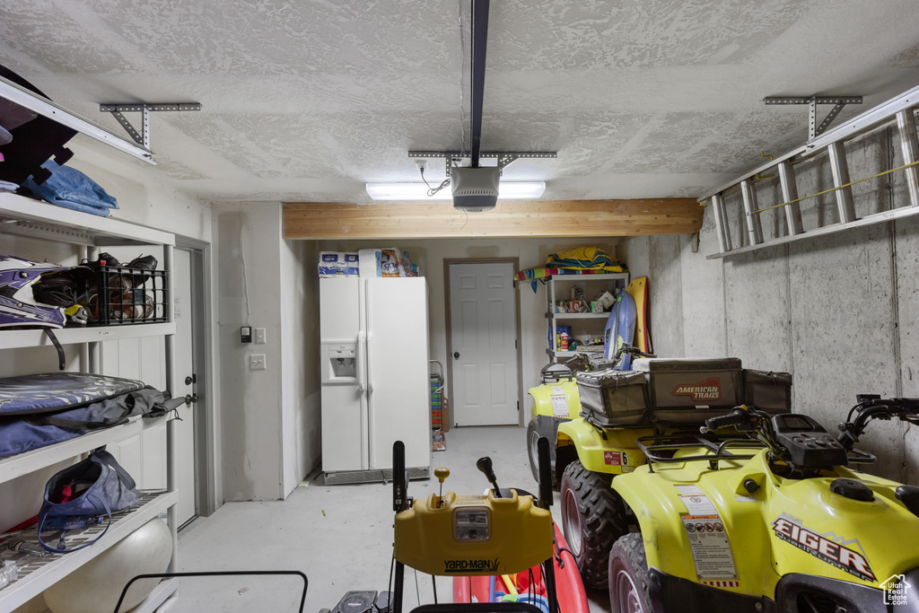 Garage with white refrigerator with ice dispenser and a garage door opener