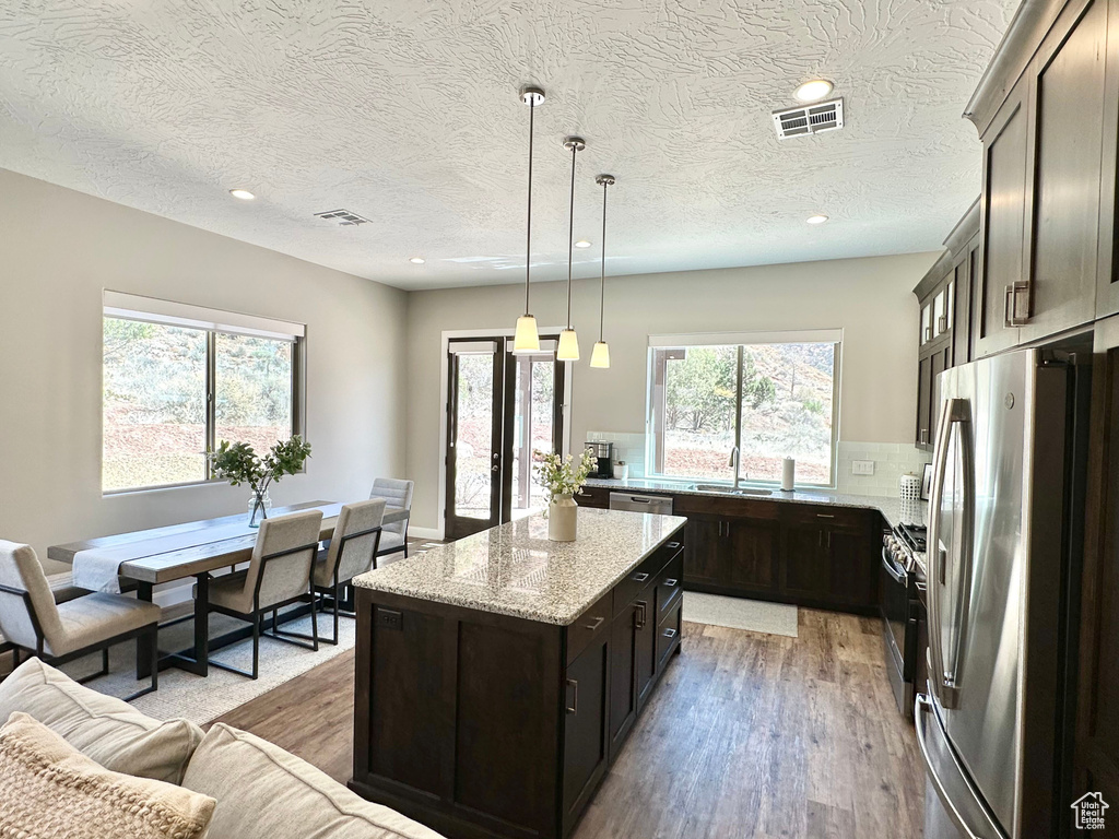 Kitchen with stainless steel appliances, light wood-style flooring, a kitchen island, light stone countertops, and recessed lighting