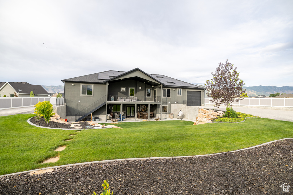 Rear view of house with stairs, roof mounted solar panels, a patio, a deck with mountain view, and an attached garage