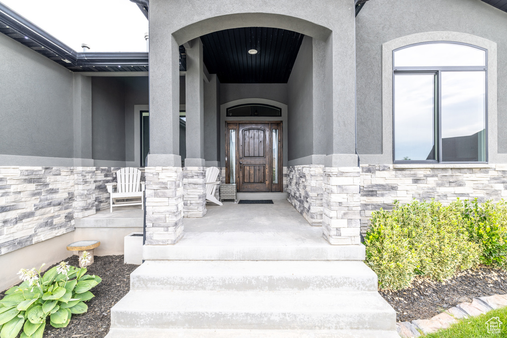 Doorway to property with stucco siding, stone siding, and a porch