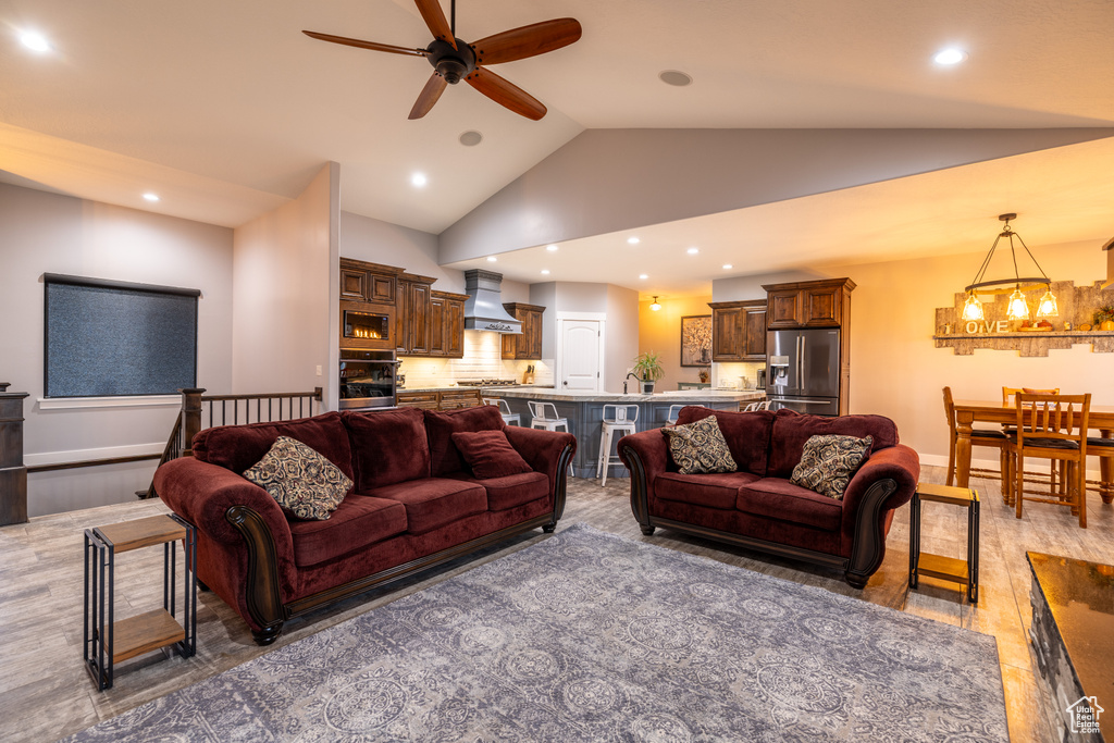 Living area with ceiling fan, a chandelier, vaulted ceiling, recessed lighting, and light wood-style flooring