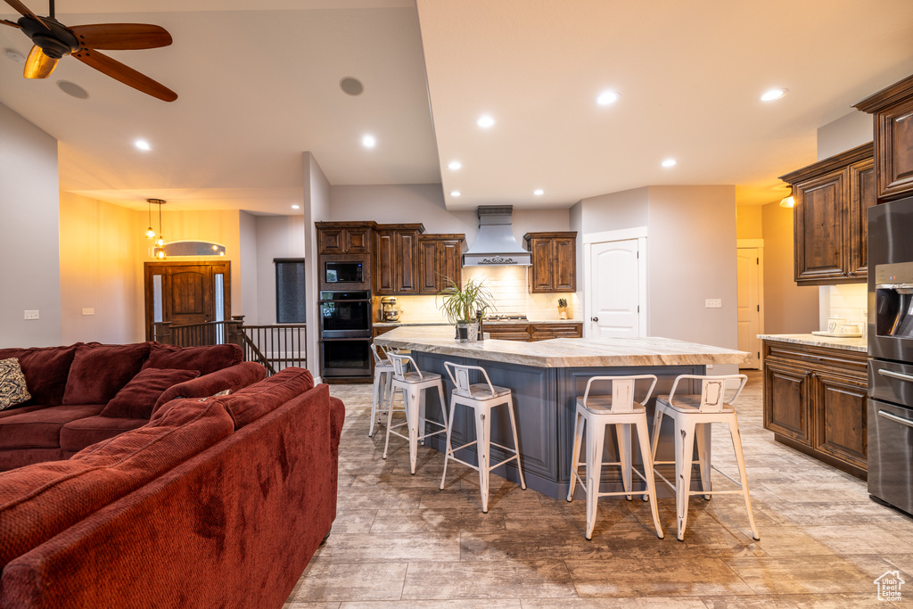 Kitchen featuring custom range hood, black appliances, open floor plan, light countertops, and a large island