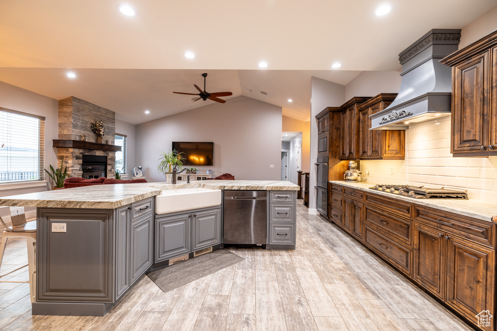 Kitchen with stainless steel appliances, a stone fireplace, ceiling fan, open floor plan, and gray cabinets