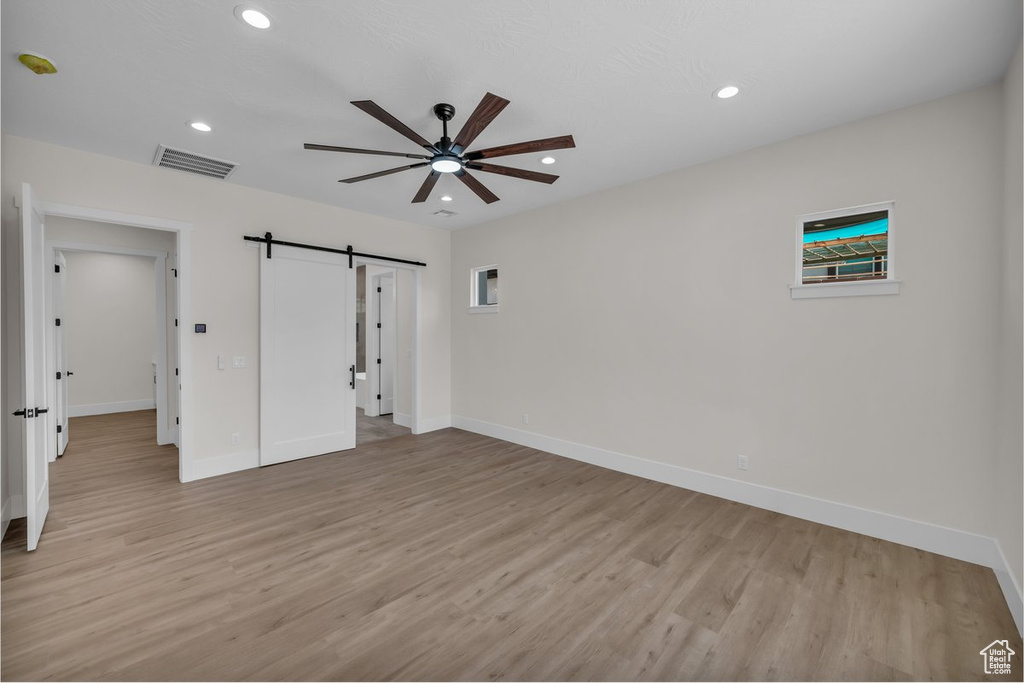 Unfurnished bedroom featuring a barn door, light wood finished floors, recessed lighting, and ceiling fan
