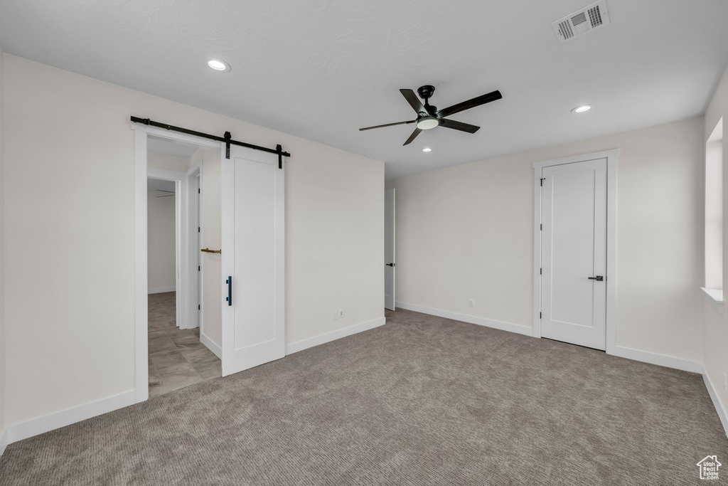 Unfurnished bedroom featuring carpet flooring, a barn door, recessed lighting, and a ceiling fan